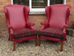 A pair of Parker Knoll wingback armchairs. A pair of Parker Knoll wingback armchairs, covered in a claret-coloured faux leather with contrasting tartan fabric used on the seat cushions.